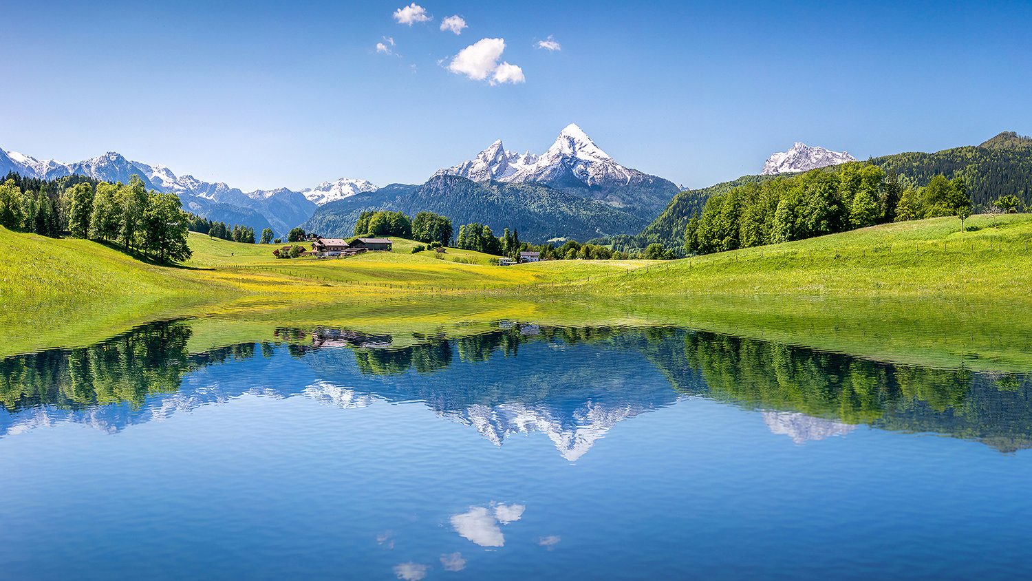 Berglandschaft mit grünen Wiesen und einem See, in dem sich die Berge spiegeln